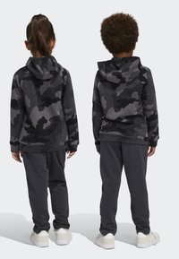 Due bambini voltano le spalle, indossando felpe con cappuccio mimetiche grigie abbinate e pantaloni della tuta grigi. Il tessuto è morbido con una vestibilità comoda; le scarpe bianche completano il look.