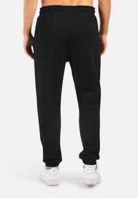 Schwarze Jogginghosen mit elastischem Bund, aus weichem Stoff, mit schmal zulaufenden Beinen und gerippten Säumen. Kombiniert mit weißen Turnschuhen mit Logo-Details.