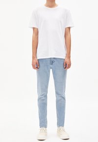 Biała koszulka z krótkim rękawem, jasnoniebieskie jeansy o dopasowanym kroju oraz beżowe tenisówki. Gładki materiał, casualowy design bez wzorów i logo.