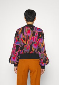 Pull tricot multicolore présentant des motifs abstraits vibrants en violet, rouge et orange, avec un ourlet côtelé noir et des manches bouffantes.