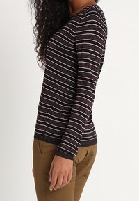 Długi rękaw z prążkowanym wzorem i dekoltem w szpic. Ciemne tło z jasnymi poziomymi paskami. Miękki, teksturowany materiał. Wąski krój.