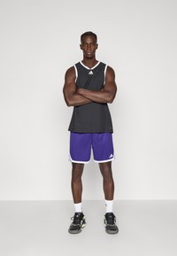 Μαύρο αθλητικό τοπ χωρίς μανίκια με λευκές λεπτομέρειες, σετ με μωβ σορτς με λευκή επένδυση και μαύρα αθλητικά παπούτσια. Απλός σχεδιασμός.