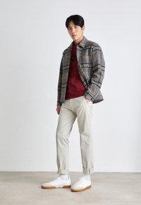Gray plaid shirt jacket over a maroon t-shirt, light beige trousers, and white sneakers with gum soles. Smooth textures, casual fit.