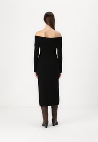 Vestido preto de malha, com um ombro à mostra, mangas longas, design ajustado e textura canelada na gola; usado com botas castanhas até ao joelho.