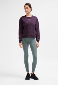 Lila sweatshirt med långa ärmar och rund halsringning, kombinerad med ljusgröna leggings och svarta träningsskor. Slät textur, avslappnad passform.