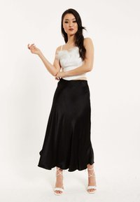 White top with feather accents, black satin skirt, and white strappy heels. The skirt flows to ankle length with subtle sheen and soft texture.