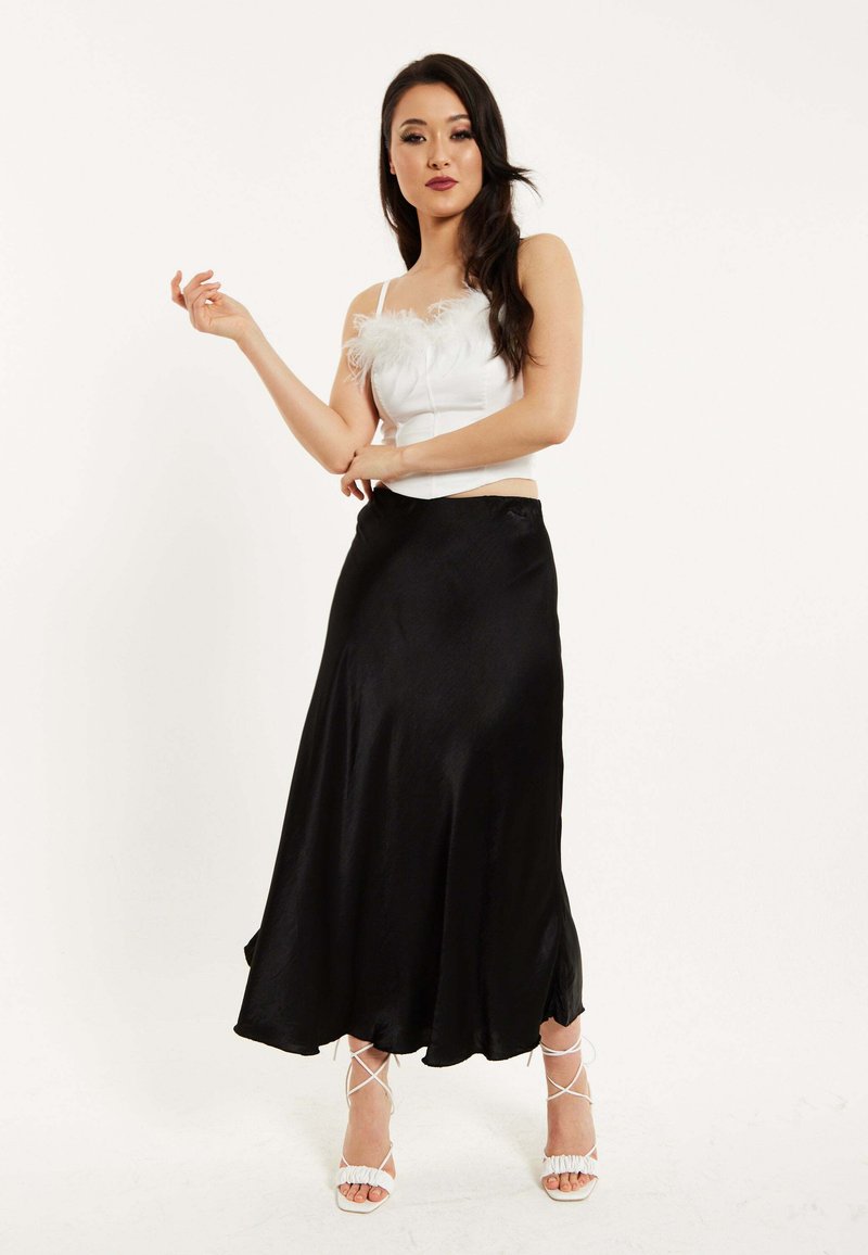 White top with feather accents, black satin skirt, and white strappy heels. The skirt flows to ankle length with subtle sheen and soft texture.