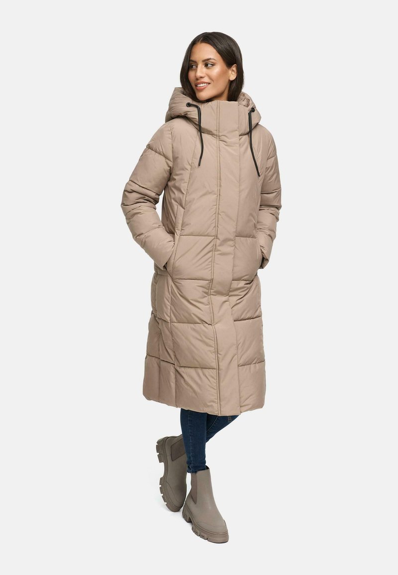 Beige pufferjakke med hætte, med lynlås foran, quiltet design og to sidelommer. Båret over blå jeans og grå ankelstøvler.