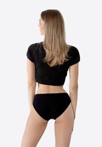 Top nero corto e mutande alte in vita nere su una modella femminile, caratterizzati da un tessuto liscio e un design elegante, mostrati di spalle.