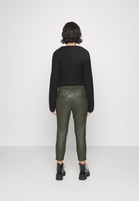 Pull en tricot noir court à manches longues accompagné d'un pantalon tapered en simili cuir olive. Des bottines noires à lacets viennent compléter le look.