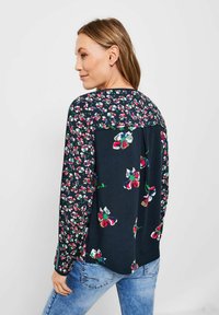 Blusa floreale con maniche lunghe, base blu navy e motivi di fiori multicolori. Tessuto morbido, orlo arrotondato e vestibilità rilassata.