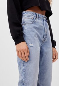 Ljusblå denimjeans med hög midja, med slitna detaljer och en avslappnad passform. Tillsammans med en croppad svart sweatshirt.