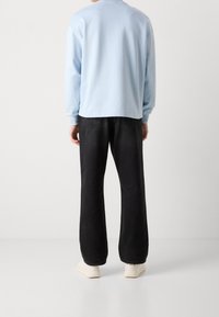 Felpa a maniche lunghe azzurro chiaro con vestibilità comoda, abbinata a jeans ampi neri e sneakers crema. Tessuto liscio, senza motivi visibili.