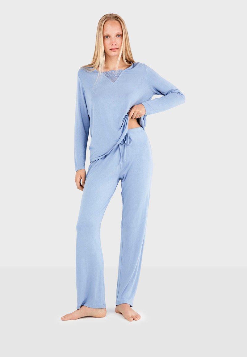 Ensemble de loungewear bleu clair comprenant un haut à manches longues avec des détails en dentelle et un pantalon avec cordon de serrage ; tissu doux avec une coupe décontractée.