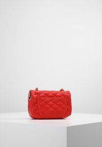 Borsa trapuntata rossa con forma rettangolare, dotata di una tasca frontale, finiture in oro e una tracolla corta a catena. Texture liscia.