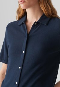 Camicia a maniche corte con bottoni di colore navy, realizzata in tessuto testurizzato. Presenta un colletto, una fila di bottoni bianchi e una vestibilità comoda.