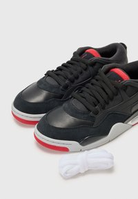 Baskets noires en suède et cuir, avec des accents rouges, une semelle en caoutchouc blanche et des lacets blancs assortis.