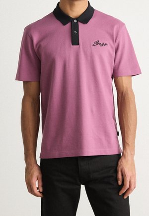 T-paita tummanpunaisesta puuvillasta mustalla kauluksella, jossa on napitettava edusta ja musta brodeerattu logo rinnassa. Lyhyet hihat ja normaali istuvuus.