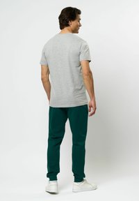 Grå bomulls t-shirt med korta ärmar tillsammans med gröna mjukisbyxor. Har elastiska muddar och en avslappnad passform. Vita sneakers kompletterar looken.