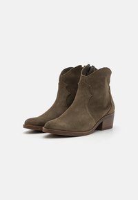 Botas de ante verde oliva hasta el tobillo con un diseño ondulado, punta afilada y tacón cuadrado bajo. Cuenta con un cierre de cremallera lateral.