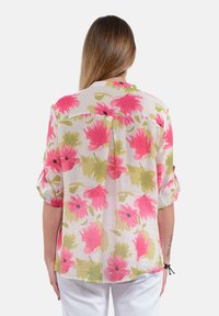 Camicia floreale in tessuto leggero, con grandi fiori rosa e verdi. Maniche corte con risvolto; dettaglio di piega sul retro; orlo arrotondato.