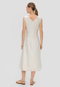 Robe sans manches en V blanche avec des rayures verticales jaunes. Forme évasée, longueur genou, dotée d'une fermeture éclair dans le dos et de sandales simples.