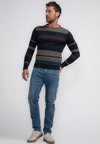 Pulover raiat în nuanțe de navy, gri și burgundy, cu guler și manșete ribbate. Asortat cu blugi deschiși la culoare și adidași gri.