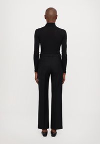 Svart långärmad topp med hög krage och subtila dekorationer, ihop med högmidjade svarta byxor med rak bendesign.