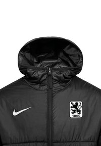 Zwarte gewatteerde jas met hoge kraag, voorzien van een rits voorkant en een Nike-logo. Toont een wit leeuwenembleem met "1860" op de borst.