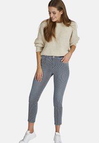 Crème ribbelgebreide trui gecombineerd met navy en witte gestreepte cropped jeans. Witte sneakers maken de look compleet. Eenvoudig ontwerp en casual stijl.