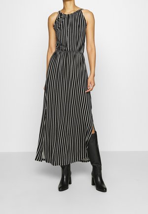 Vestido midi sin mangas negro con rayas verticales blancas, combinado con botas negras de tacón hasta la rodilla, modelo posando sobre fondo liso.