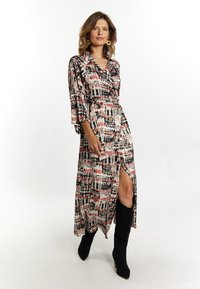 Rochie lungă, de tip wrap, cu un model abstract multicolor, având o fante adâncă și mâneci până la cot, combinată cu cizme negre până la genunchi.