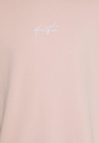 Helles pinkes T-Shirt aus weichem Stoff mit Rundhalsausschnitt und gesticktem "Your Turn"-Text in Weiß auf der Brust. Glatte Textur.