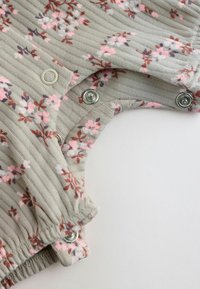 Mehka siva rebrasta tkanina z rožnatim in rjavim cvetličnim potiskom, ki ima kovinske pritisne gumbe in elastičen manšest na otroški oblačilu.