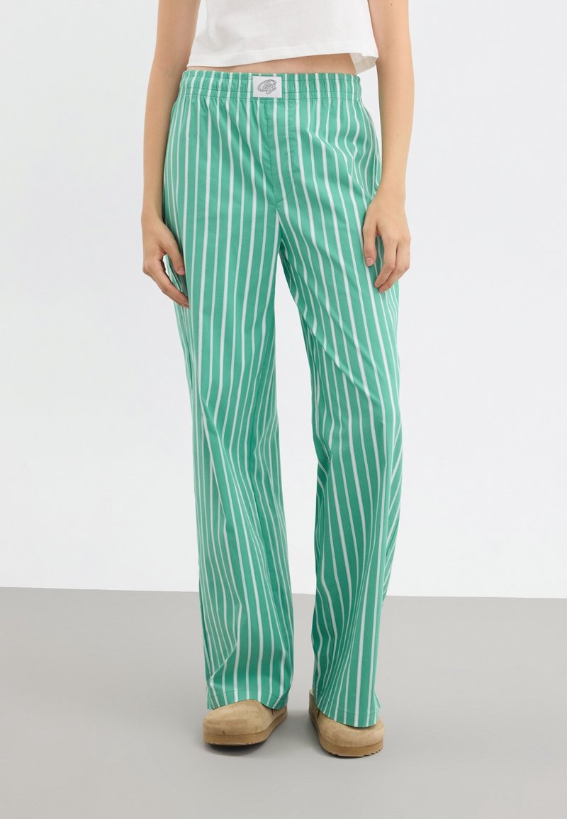 Pantalon ample à rayures verticales vertes et blanches avec taille élastique, porté avec des chaussures beiges et un haut blanc court.