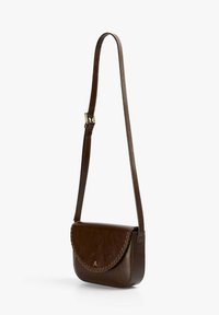 Sac bandoulière en cuir brun foncé avec rabat cousu et bandoulière réglable suspendu sur un fond blanc.