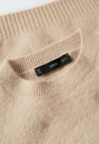 Maglione beige lavorato a maglia con colletto rotondo a coste, caratterizzato da una texture morbida e un'etichetta cucita nel collo con informazioni sul marchio e sulla cura.