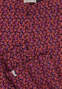 Paarse stof met een abstract patroon in oranje en roze. Inclusief een label met de tekst "LOOXS" en "REVOLUTION". Glad van textuur, lichtgewicht materiaal.