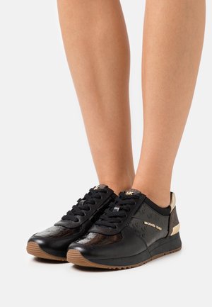 Sneaker in pelle nera con punta lucida, dettagli dorati, lati texture e suola in gomma marrone. Design con lacci per una vestibilità sicura.