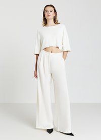 Top bianco corto con una vestibilità ampia, abbinato a pantaloni bianchi a vita alta e a gamba larga. Tacchi neri a punta completano l'outfit.