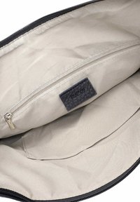 Bēšas auduma somas iekšpuse ar kabatu, kas aiztaisāma ar rāvējslēdzēju, un uz kuras ir melnas ādas etiķete ar izspiestu uzrakstu „RUE 09”.