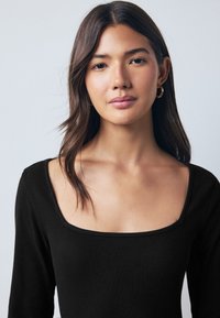 Top negro de manga larga con textura acanalada y escote cuadrado amplio. Presenta un diseño ajustado y una textura suave que realza la silueta del cuerpo.