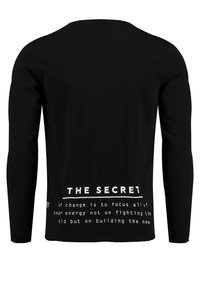 Schwarzes Langarmshirt aus glattem Stoff, mit weißem Text auf dem Rücken: "DAS GEHEIMNIS der Veränderung besteht darin, all deine Energie zu konzentrieren..."