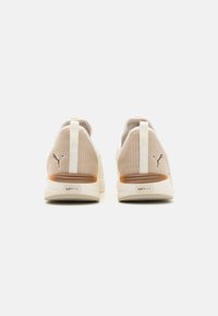 Beige athletic shoes with a mesh upper, soft cushioning, and a white sole. Features a brown accent on the heel and branding on the back.