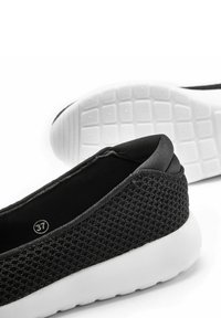Le scarpe da atletica nere presentano una tomaia in mesh testurizzato con colletto imbottito e una suola in gomma bianca, contrassegnata dalla taglia 37.
