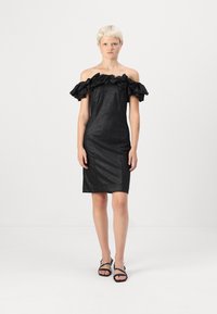 Μαύρο φόρεμα χωρίς ώμους με ραφές στη λαιμόκοψη από λαμπερό ύφασμα, εφαρμοστή σιλουέτα και μήκος μέχρι το γόνατο. Φοριέται με μαύρες σανδάλια με λουριά.