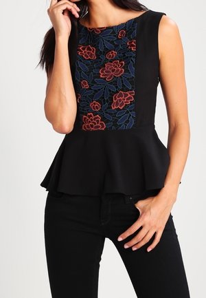 Czarny top bez rękawów z peplum i kwiatowym, czerwono-niebieskim haftowanym panelem na piersi, noszony z czarnymi spodniami.