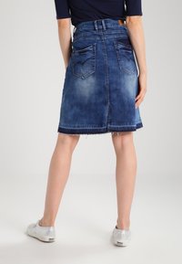 Jeanskjol med en blekt blå tvätt, A-linjeform, trasig nederkant och två bakfickor med ett zickzack-mönster. Bärs med silverfärgade sneakers.