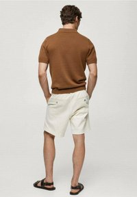 Brown knit polo shirt, cream shorts with elastic waistband, and black strappy sandals. The outfit has a casual, relaxed fit.