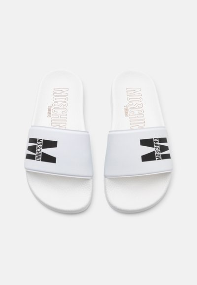 Des sandales blanches à glissière avec un coussin de pied texturé, présentant un logo noir sur une large sangle. Le design est minimaliste et contemporain.